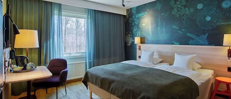 Habitación de hotel con una cama grande, un escritorio con silla, una mesita y una ventana con cortinas.