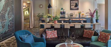 A modern lobby with a leather sofa, two armchairs, a coffee bar, and a map on the wall.