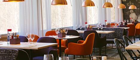 A restaurant with tables set for dining, featuring pendant lighting and a view of the outdoors.