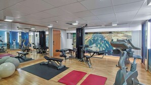 Un gimnasio con diversos equipos de ejercicio, incluyendo cintas de correr, bicicletas estáticas y máquinas de pesas.
