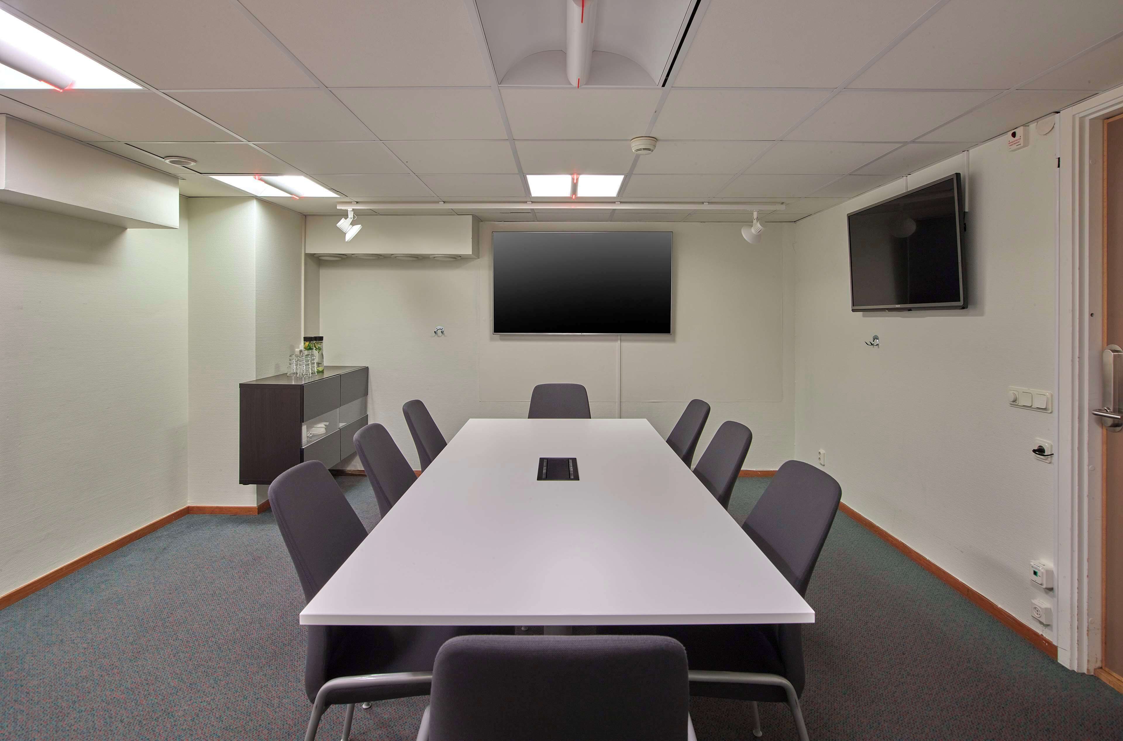 Una sala de conferencias con una larga mesa, ocho sillas, un televisor de pantalla plana y una pizarra.