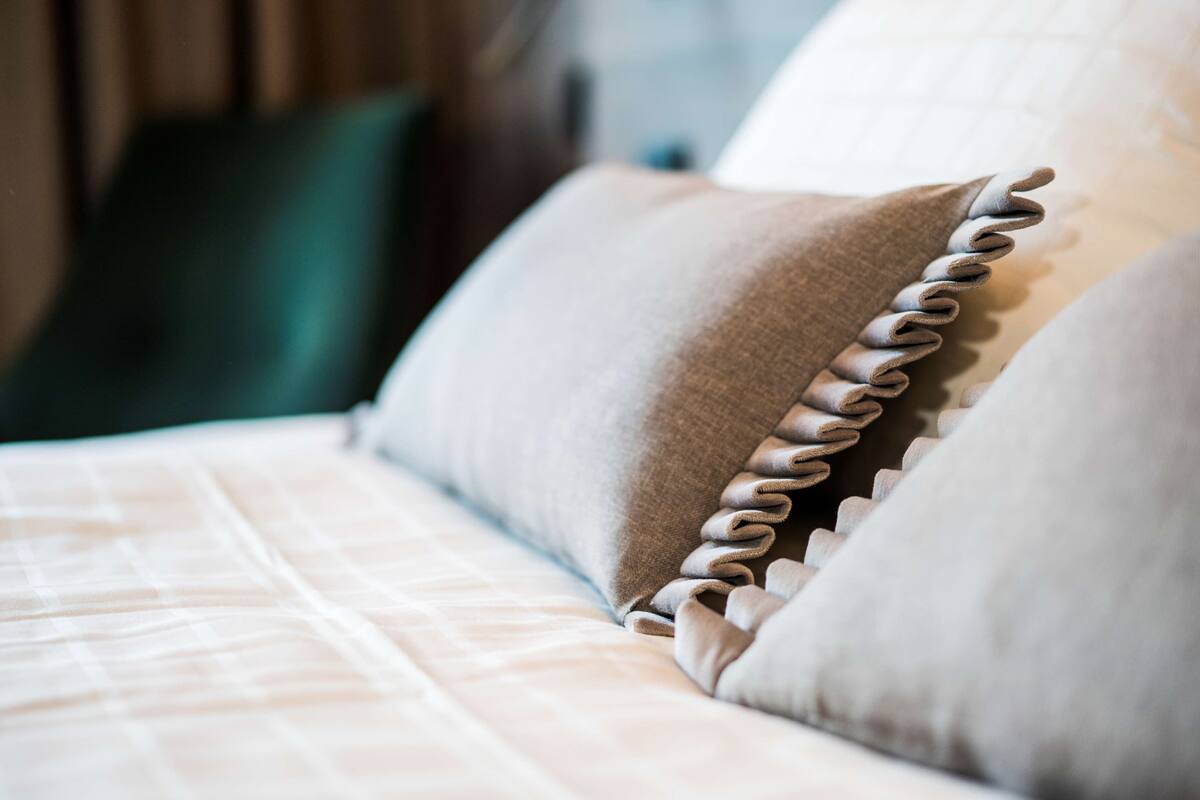 A close-up of a bed with a neatly arranged pillow and a pillow with a ruffled edge.