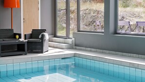 A modern indoor pool area with a clear view of the outdoors, a seating area with a lamp, and a door. - Scandic Södertälje (Sodertalje)