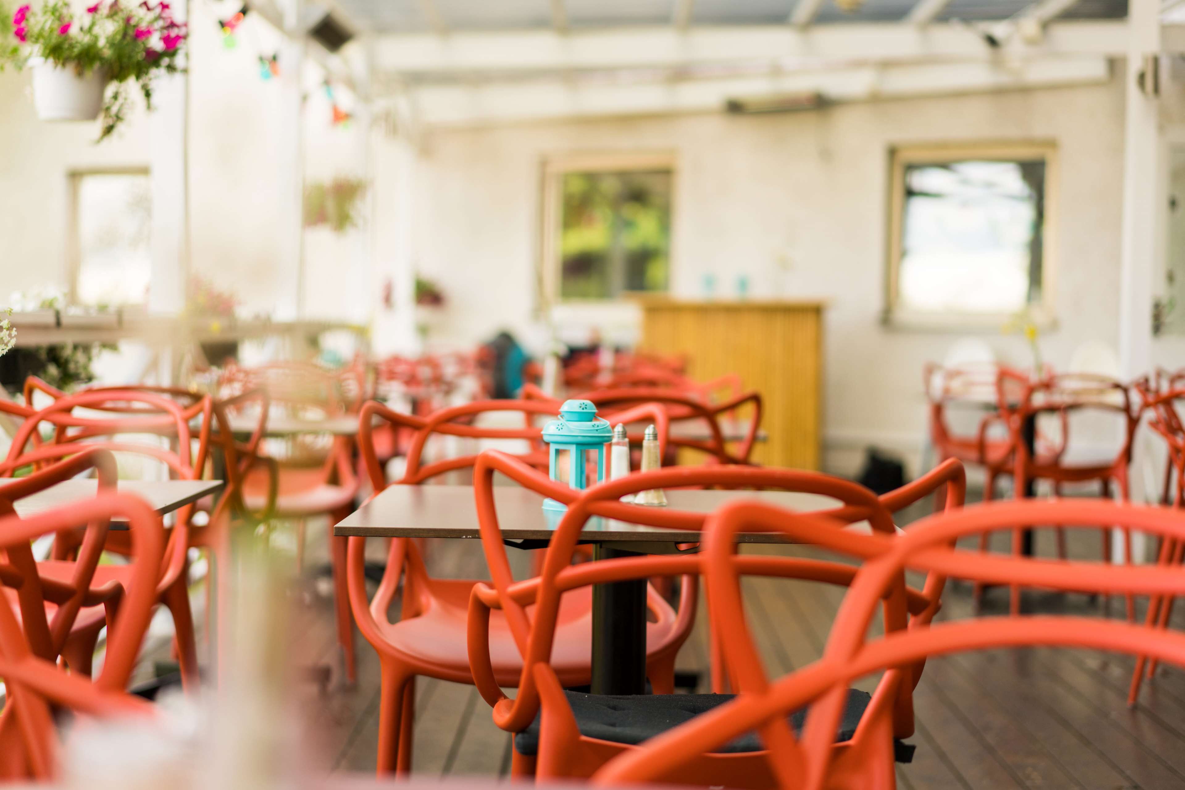 A restaurant with orange chairs and tables, a blue lantern, and hanging flowers.