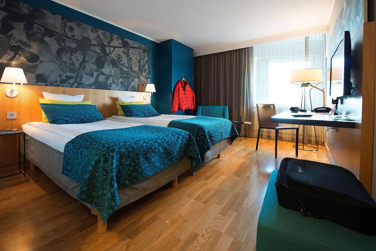 Et hotelværelse med to senge, et skrivebord, en stol, et fjernsyn og en kuffert.