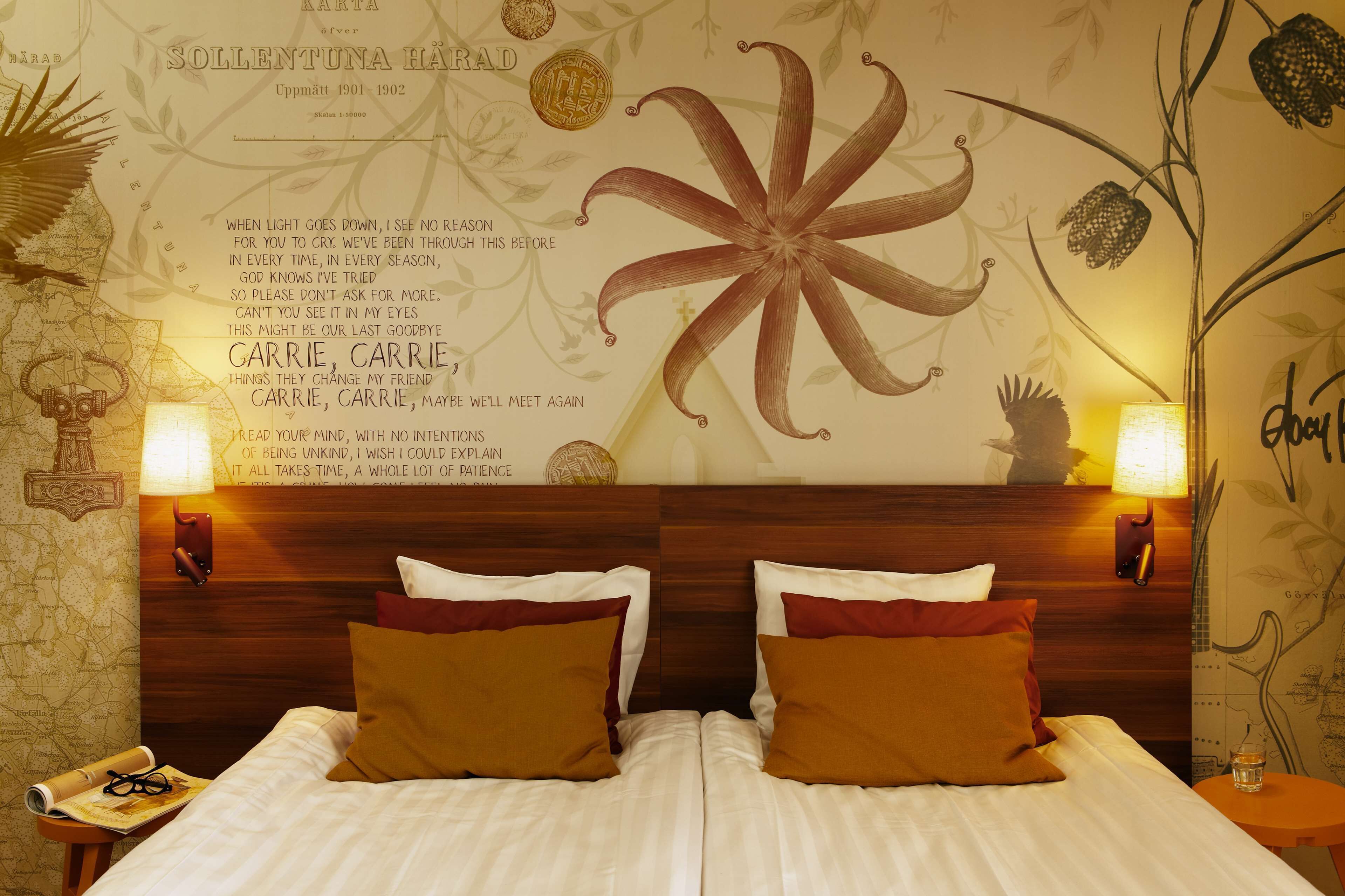 A hotel room with a bed, two bedside lamps, a wall with a large floral design, and a map on the wall.