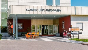 A hotel entrance with a sign reading "SCANDIC UPLANDS VÅSYBY" and a "REDUCED SPEED AHEAD" sign.