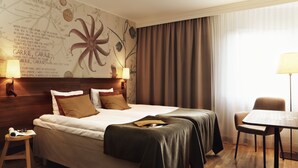 A hotel room with a large bed, two bedside lamps, a small table, and a chair.