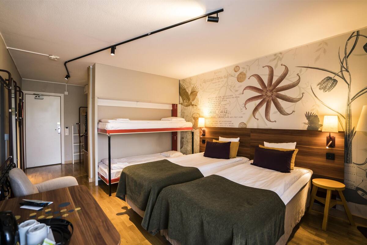 Et hotelværelse med køjesenge, et skrivebord og et vægmaleri.