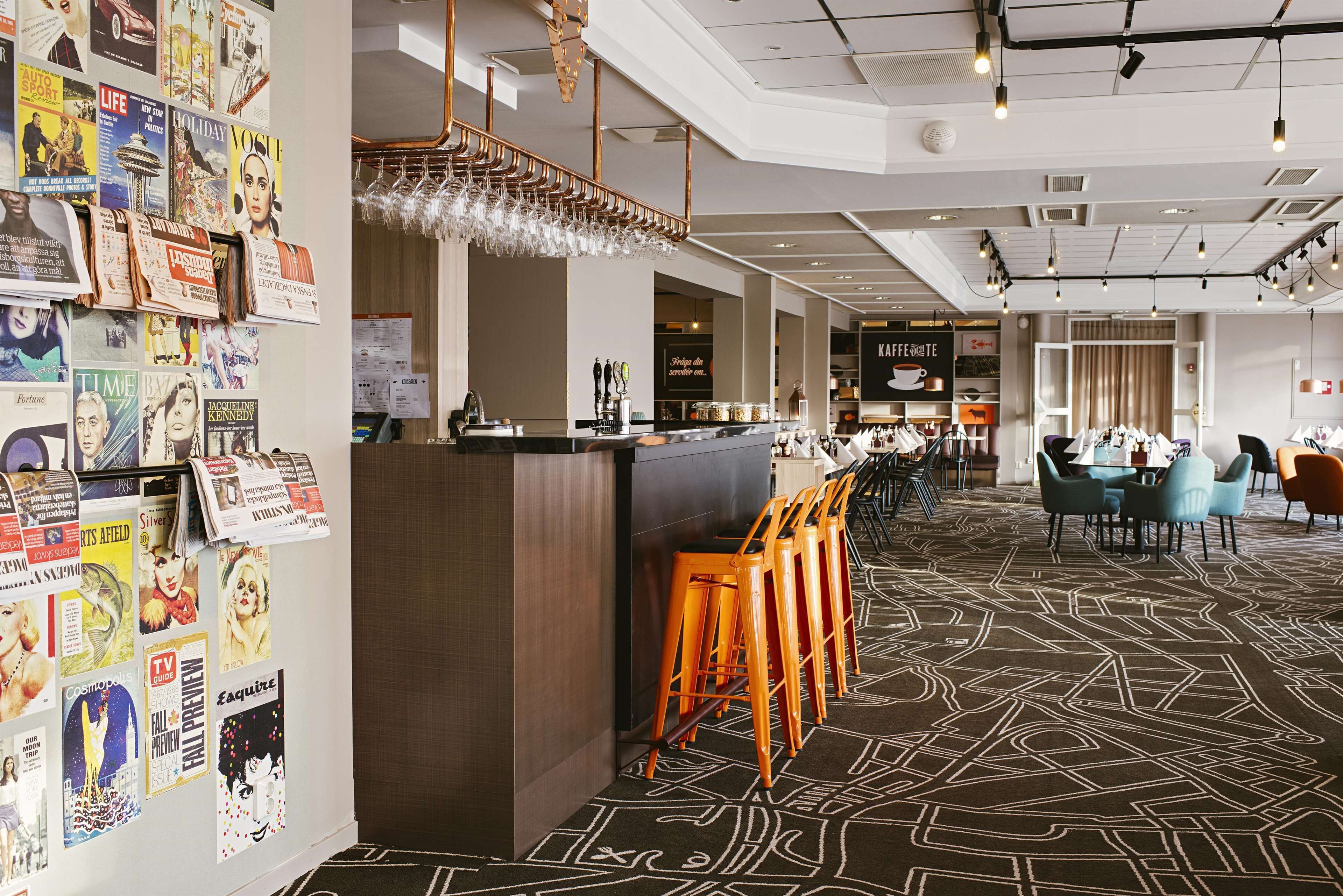 A modern hotel lobby with a bar area, seating, and a wall adorned with various magazine covers.