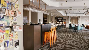 A modern hotel lobby with a bar area, seating, and a wall adorned with various magazine covers.