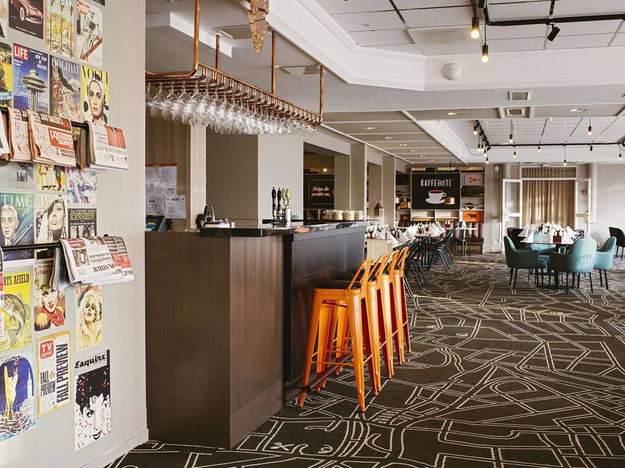 A modern hotel lobby with a bar area, seating, and a wall adorned with various magazine covers.