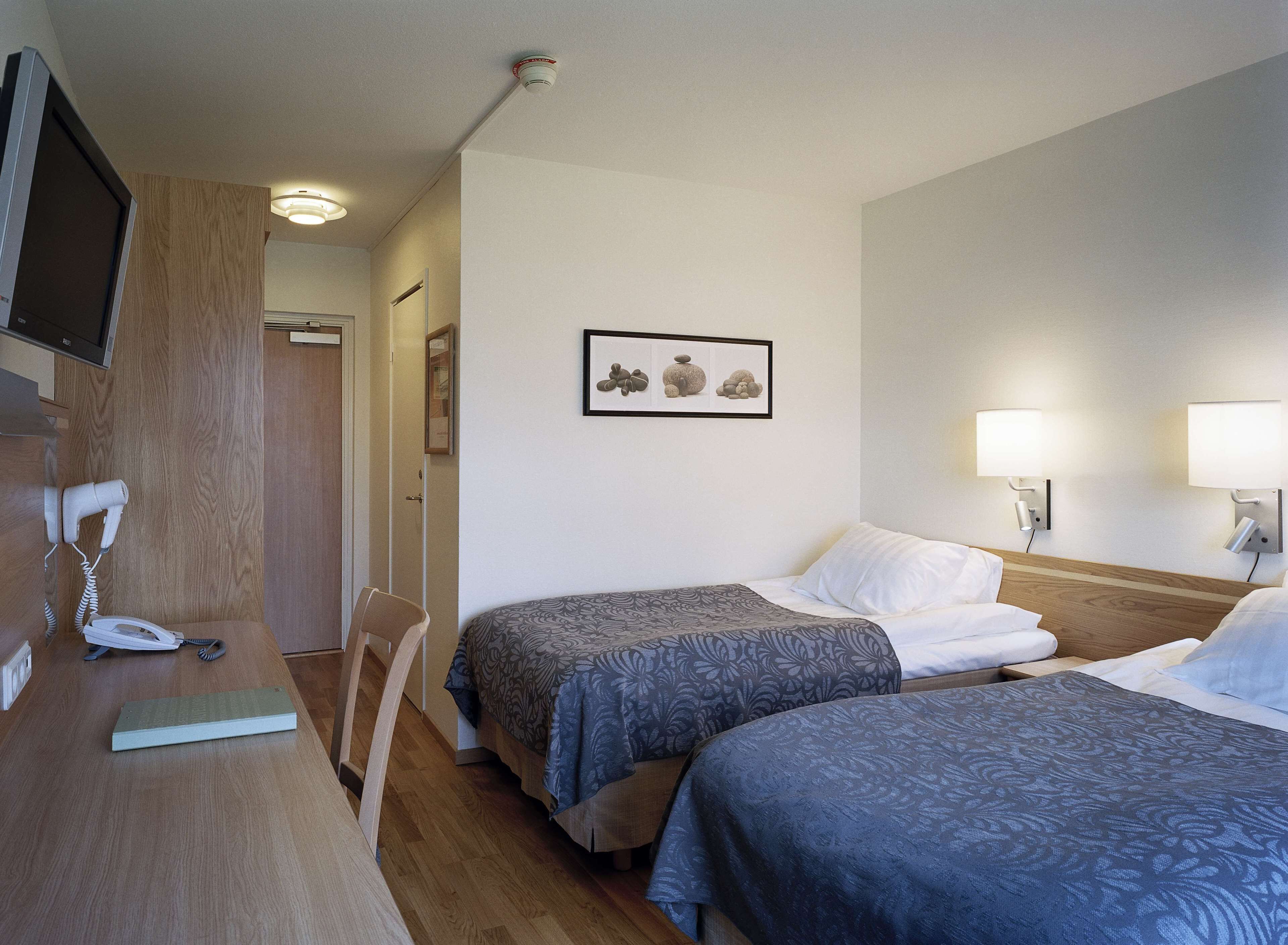A hotel room with two beds, a desk with a telephone, a TV, and a framed picture on the wall.