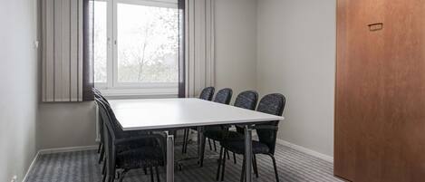 Un salón de conferencias con una gran mesa, seis sillas, un ventanal con cortinas y una puerta de madera.