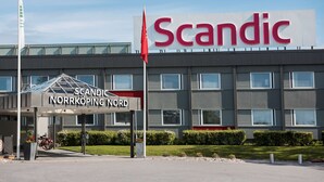 Un hotel Scandic con fachada moderna, un acceso cubierto e izado de bandera.