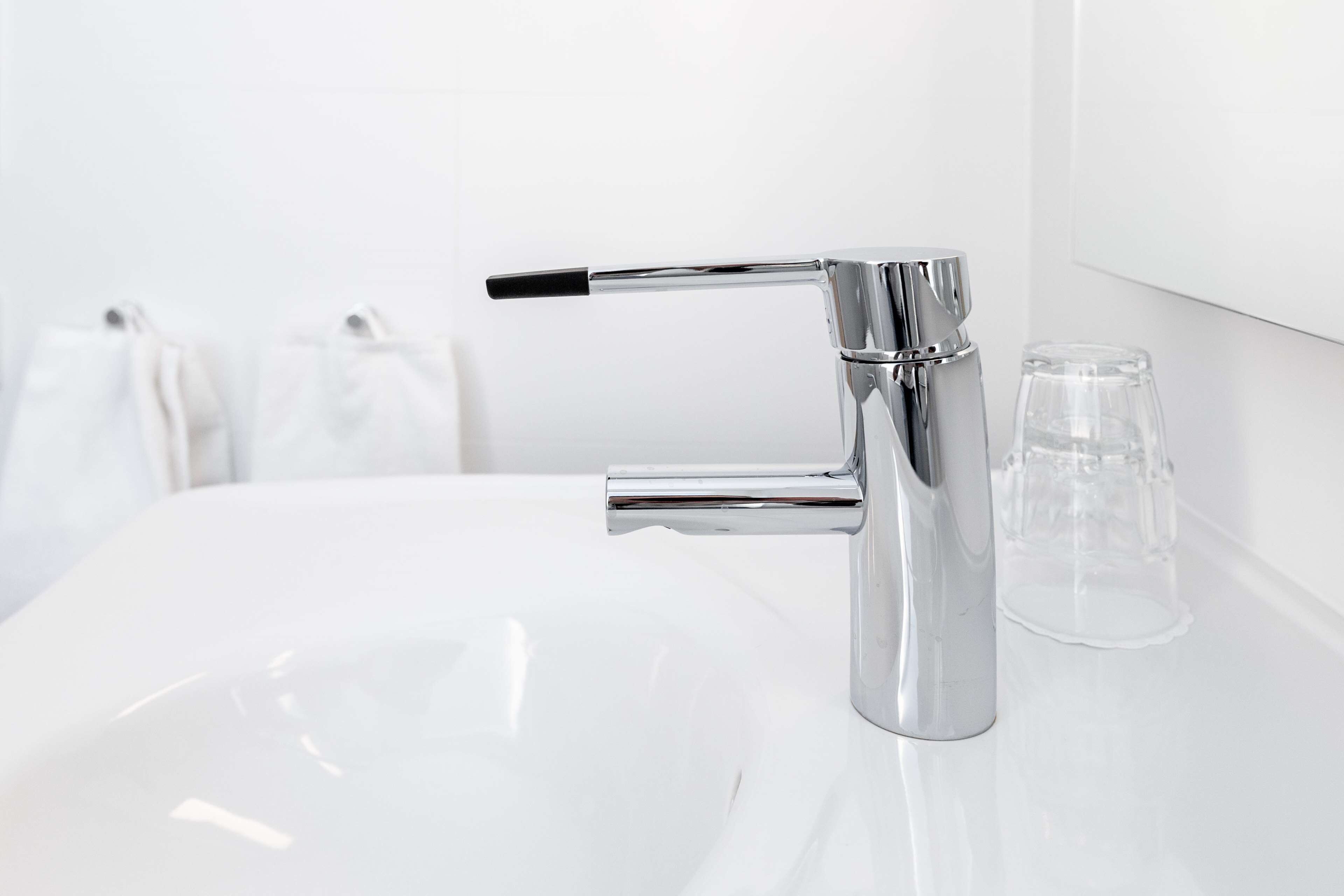 A modern bathroom with a chrome faucet, a white sink, and a clear glass.