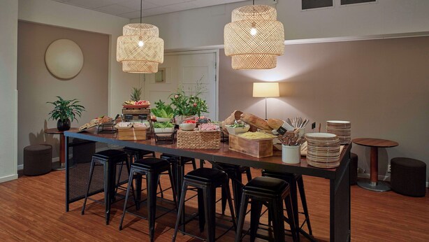 Una cocina moderna con una encimera larga, taburetes de bar, lámparas de mimbre colgantes y una planta en maceta.