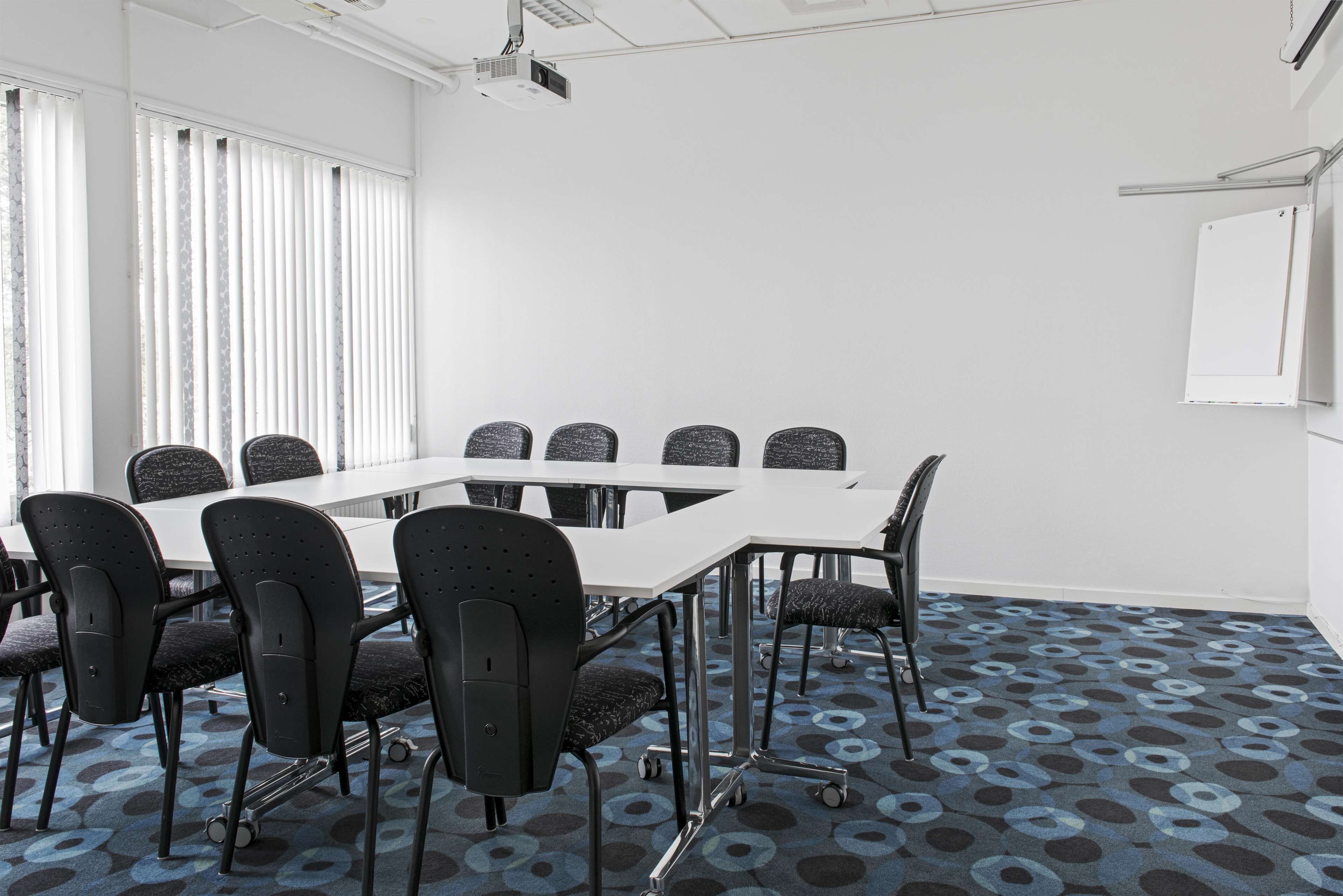Une salle de conférence avec une table blanche, des chaises noires et un tapis à motifs.