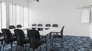Une salle de conférence avec une table blanche, des chaises noires et un tapis à motifs.
