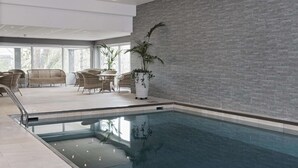 Una piscina interior con diseño moderno, rodeada de sillas de mimbre y plantas en macetas.