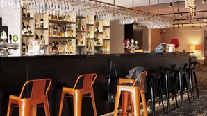 Zona de bar con varios taburetes, una barra y estantes llenos de botellas.