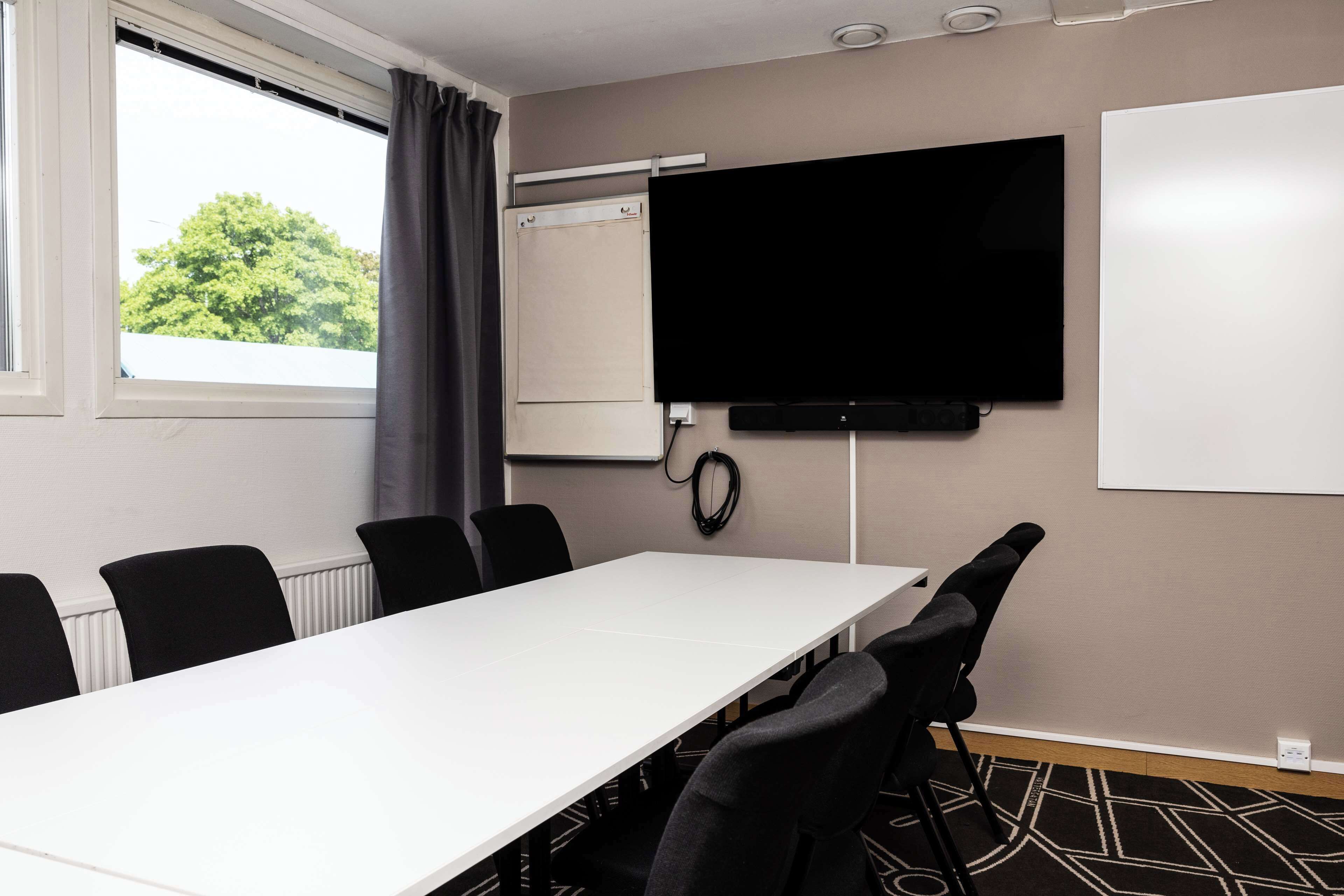 A conference room with a long table, black chairs, a whiteboard, and a TV on the wall.
