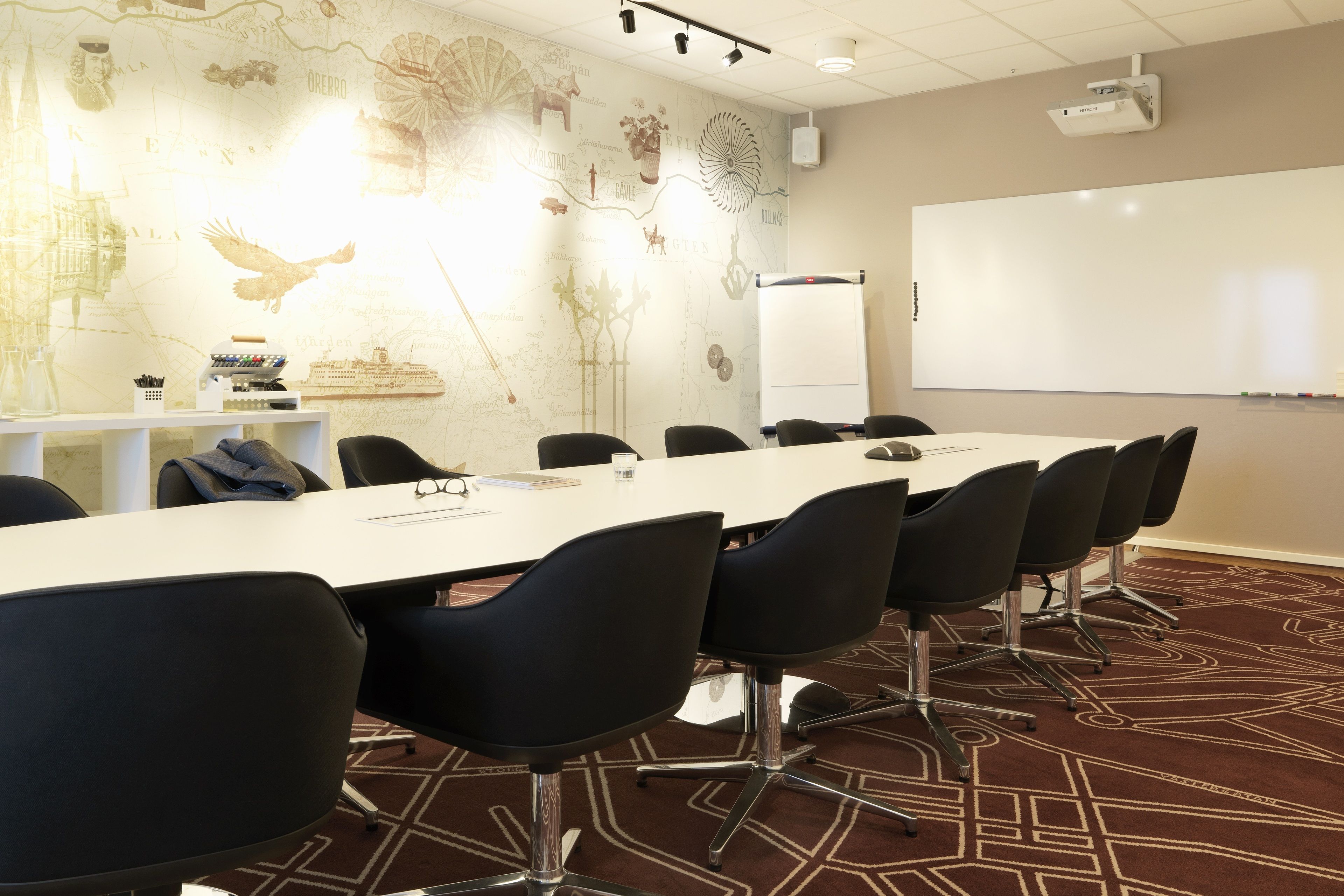 Un salón de conferencias con una mesa larga, sillas negras, una pizarra y un proyector.
