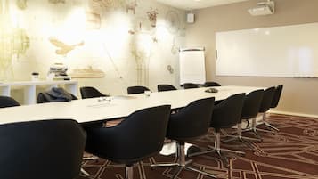 Un salón de conferencias con una mesa larga, sillas negras, una pizarra y un proyector.
