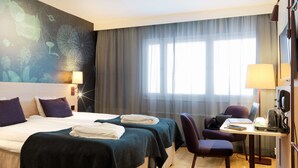 Habitación de hotel con dos camas, un escritorio con una computadora portátil, una silla y un amplio ventanal con cortinas.