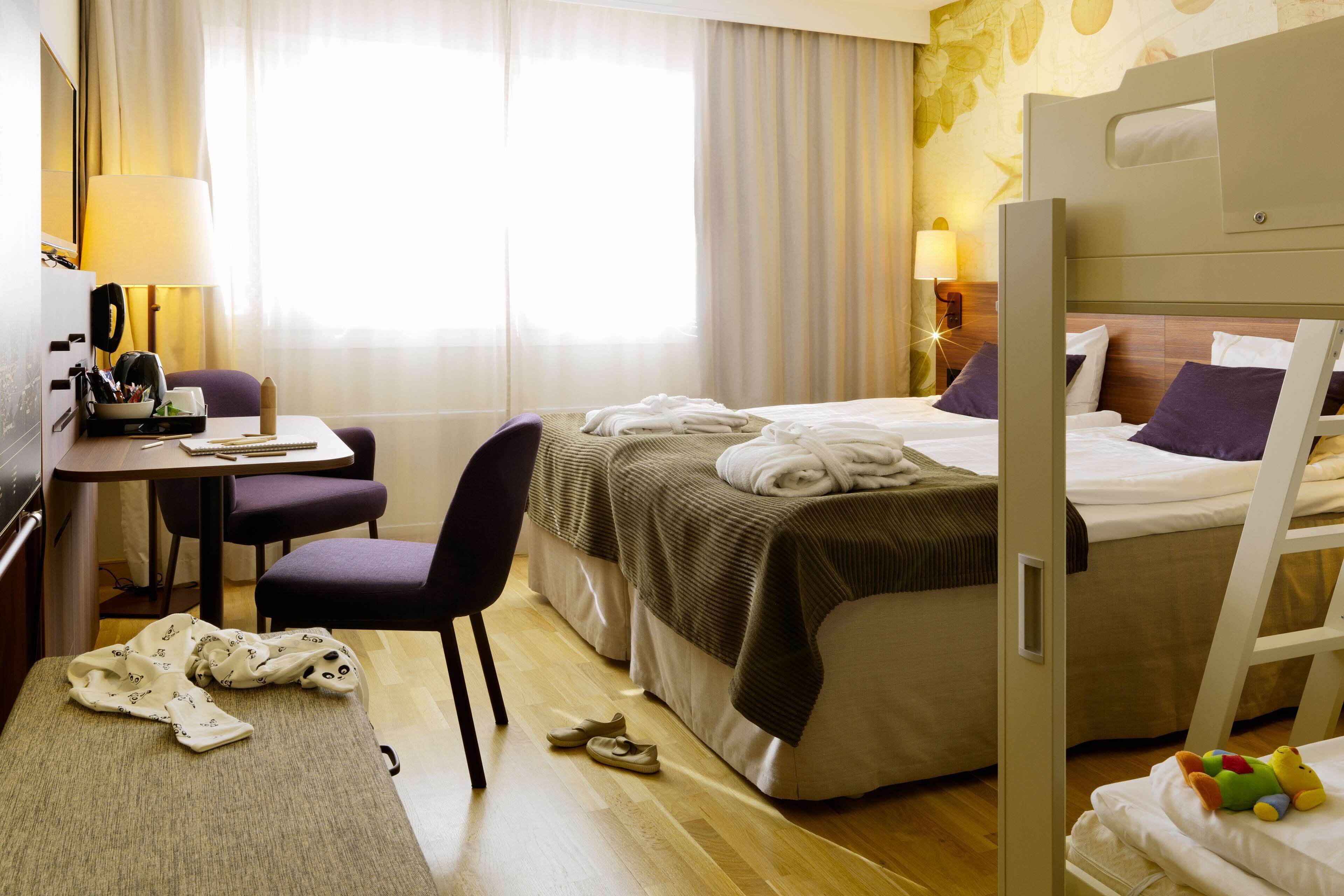 Una camera d'albergo con due letti, una scrivania, una sedia e un letto a castello.