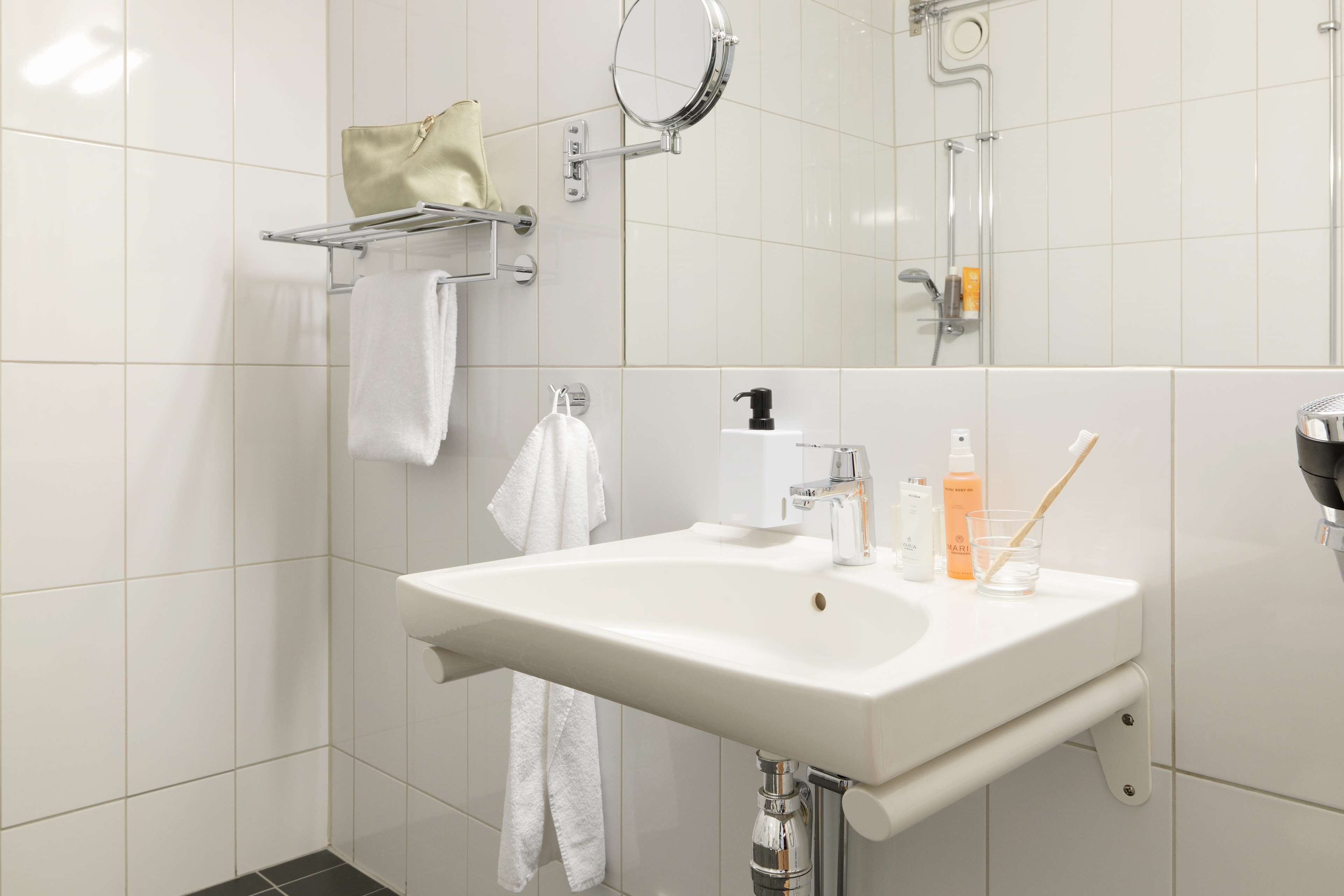Ein modernes Badezimmer mit einem weißen Waschbecken, einem Handtuchhalter mit einem beige gefärbten Handtuch, einer Duschbrause und einem Spiegel.