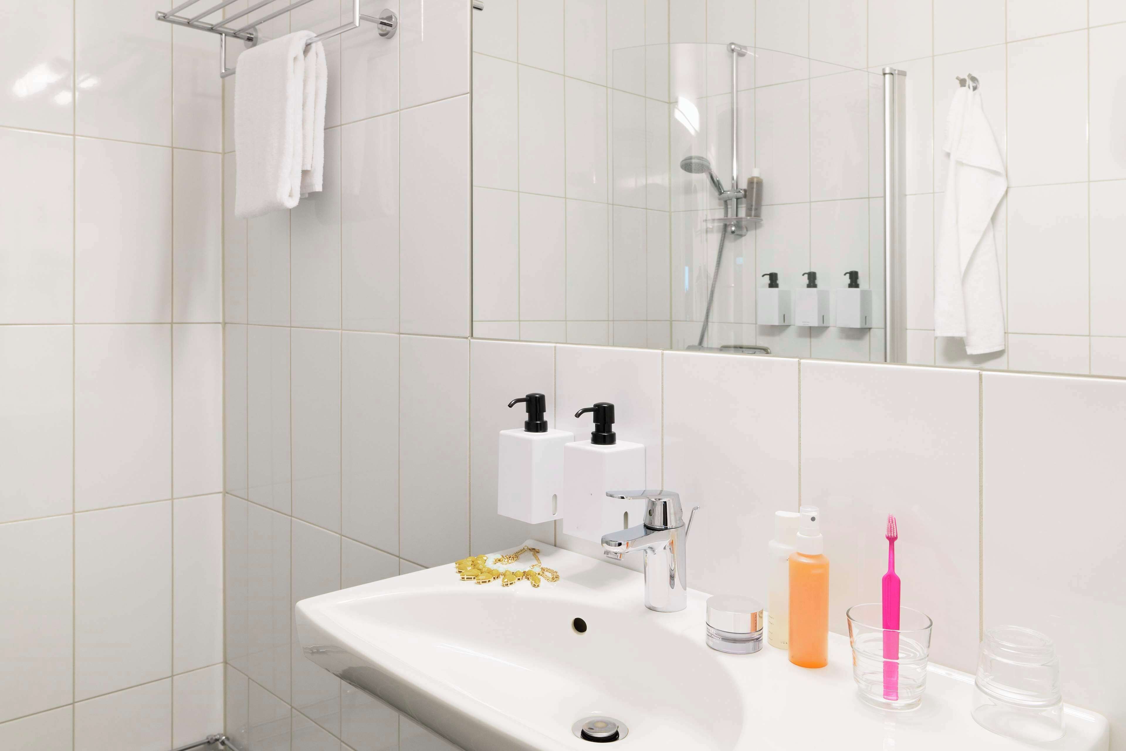 A modern bathroom with a white sink, two soap dispensers, a toothbrush, and a glass.