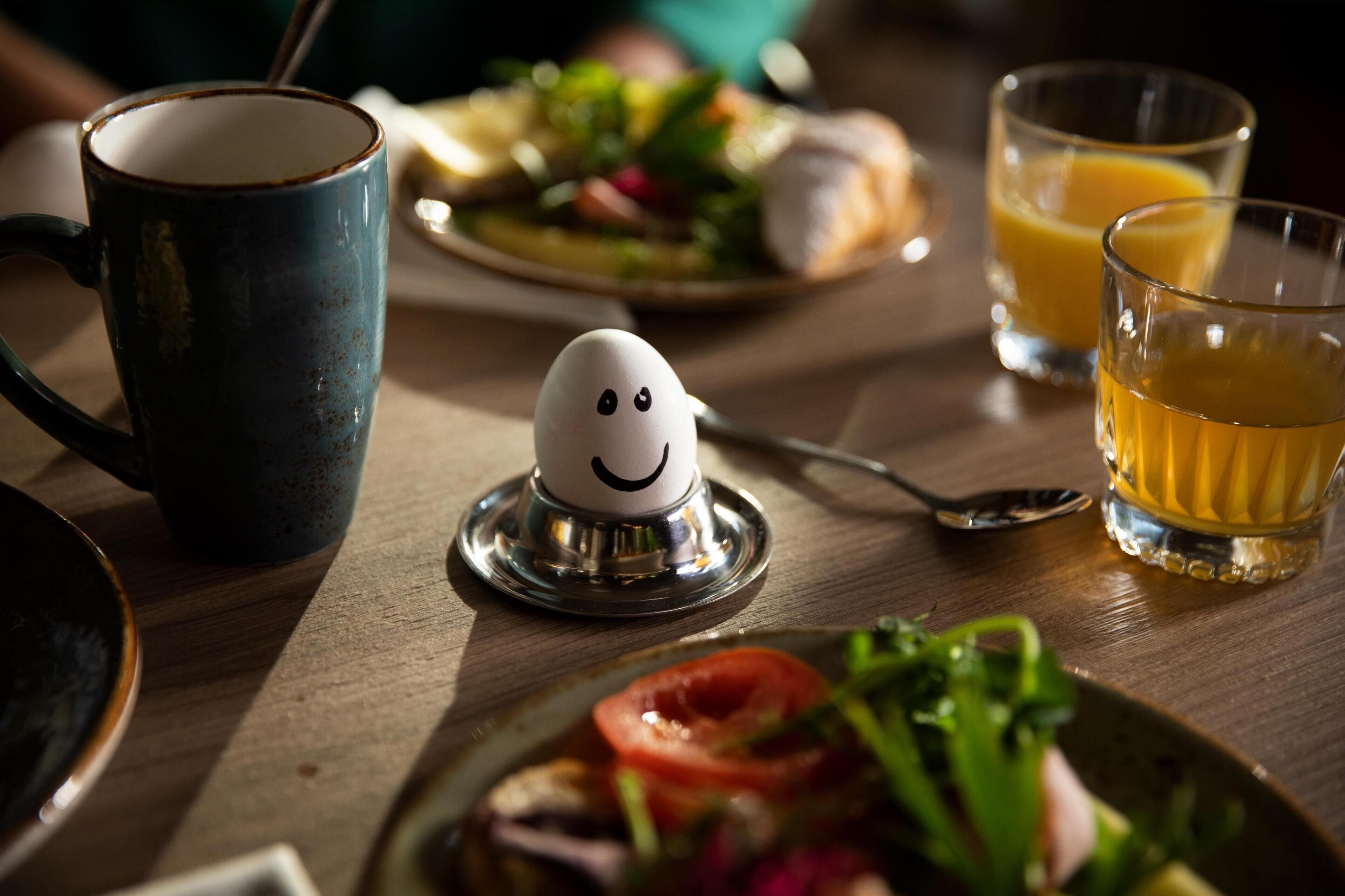 A dining table with a plate of food, a mug, a glass of orange juice, and a spoon.