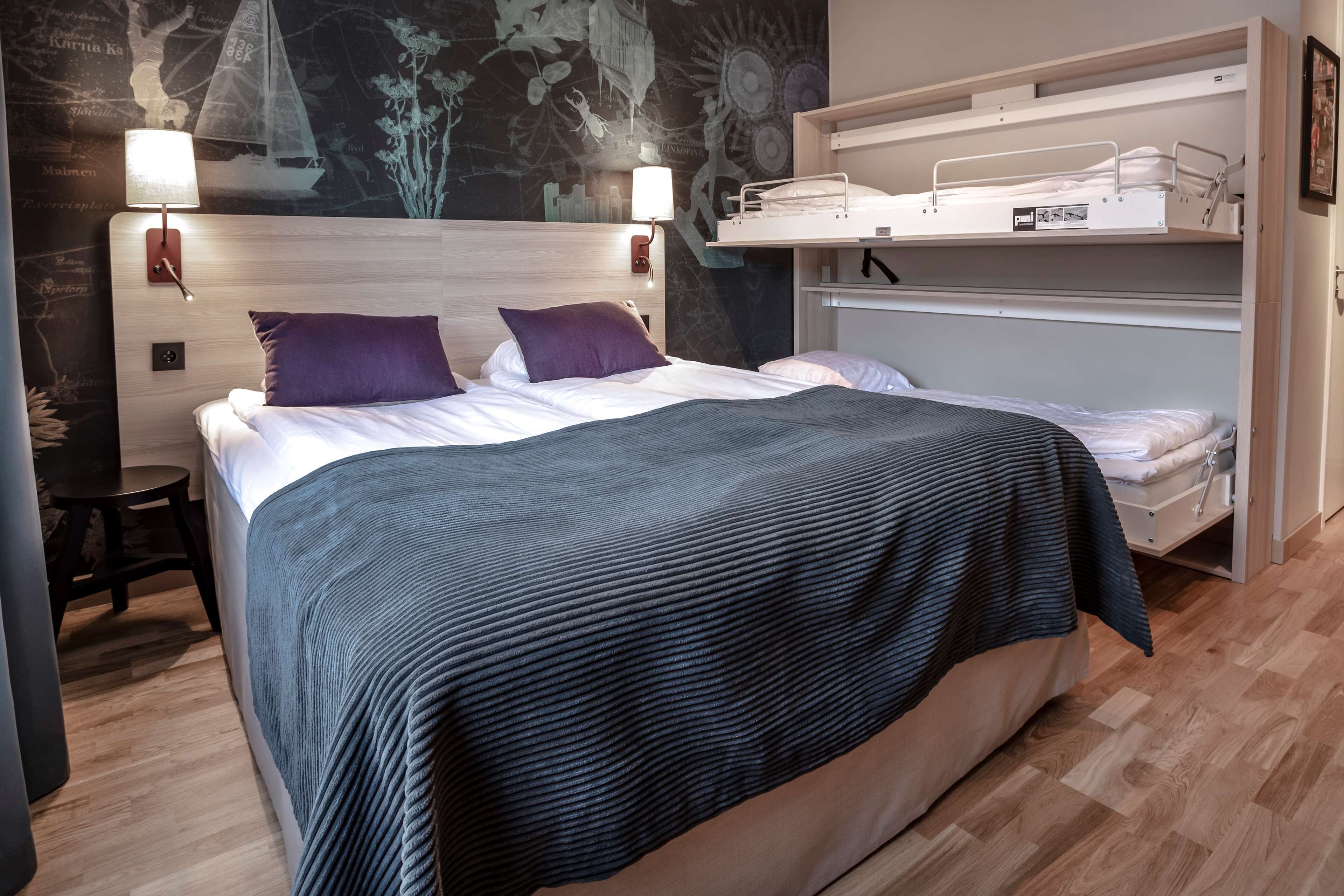 Una cama bien hecha con una colcha azul oscuro, un cabecero con luces empotradas en la pared y una cama nido a la derecha.