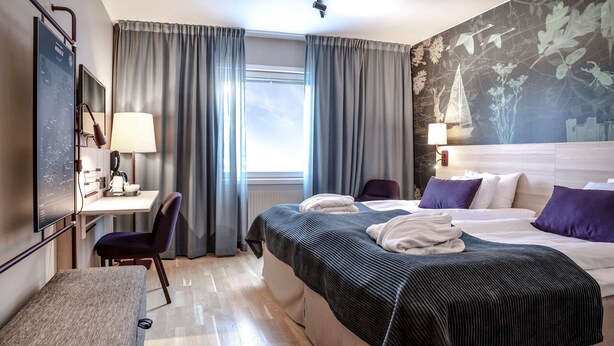 A hotel room with a bed, a desk, a chair, and a large window with curtains.
