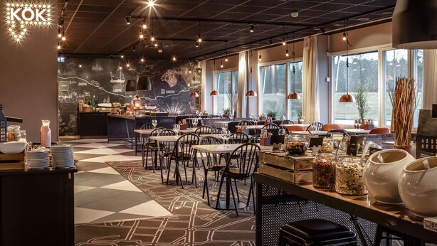 A restaurant with a modern interior, featuring a mix of tables and booths, a bar area, and a large mural on the wall. - Scandic Linköping Väst (Linkoping)