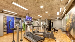 A gym with treadmills, elliptical machines, and a TV screen displaying workout videos. - Scandic Linköping Väst (Linkoping)