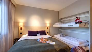 Een hotelkamer met een groot bed, twee nachtkastjes, een stapelbed en een raam met gordijnen.
