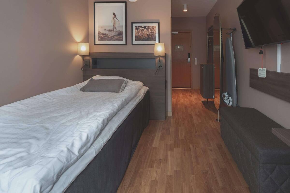 A bedroom with a bed, bedside lamps, a flat-screen TV, and a wooden floor.