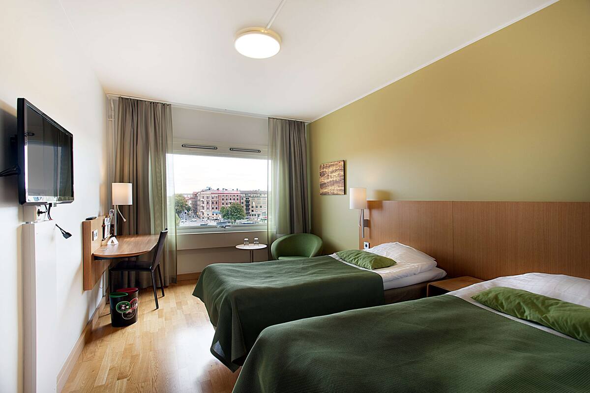 A hotel room with two beds, a desk, a chair, a TV, and a window with curtains.