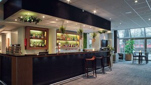 A modern bar area with a counter, bar stools, and a variety of bottles. - Scandic Hallandia (Halmstad)