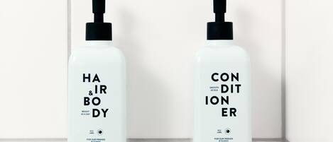 Two white bottles with black pumps, labeled "HAIR & BODY" and "CONDITIONER," hanging on a white tiled wall.