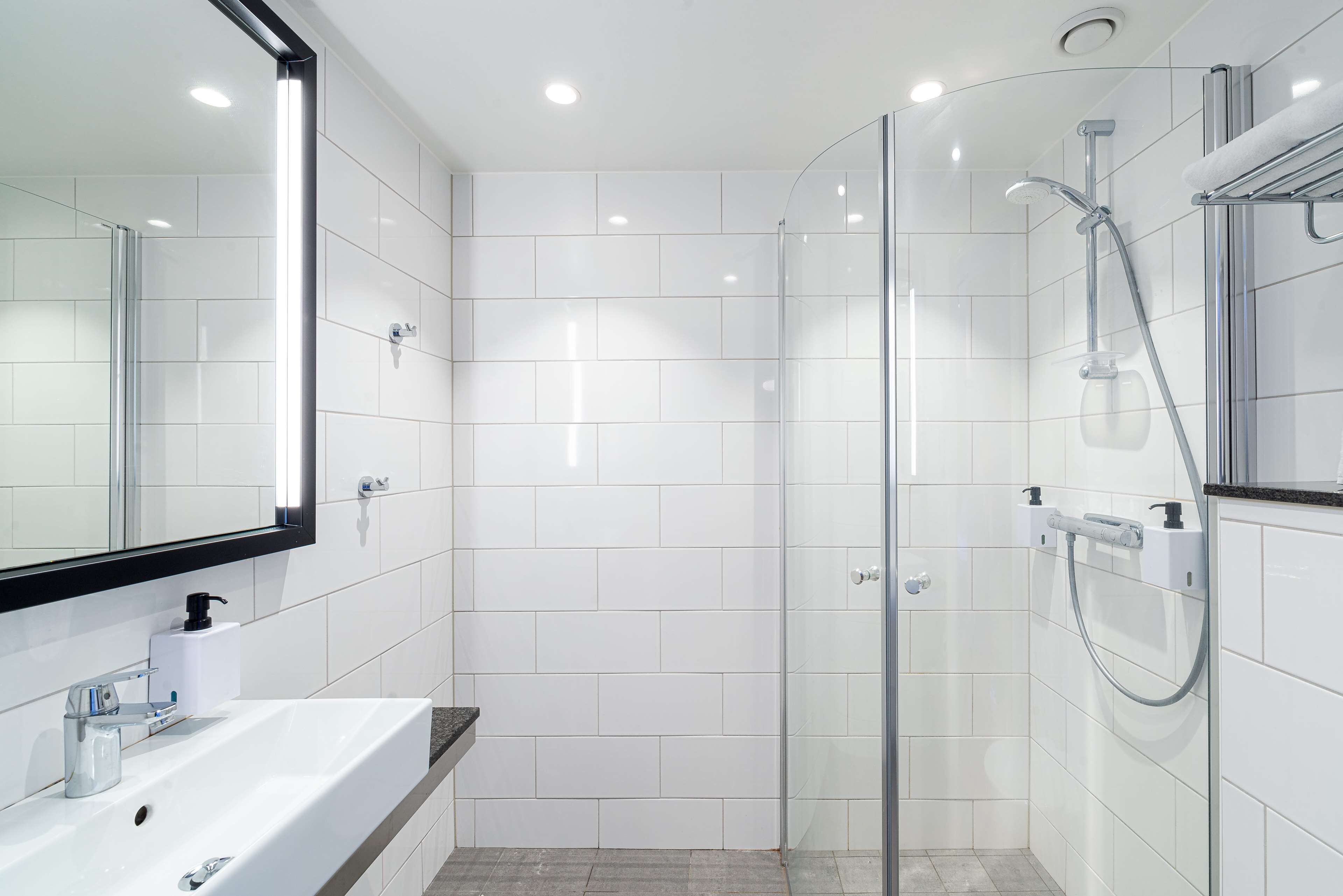 A modern bathroom with a glass-enclosed shower, a white sink with a mirror, and a towel rack.
