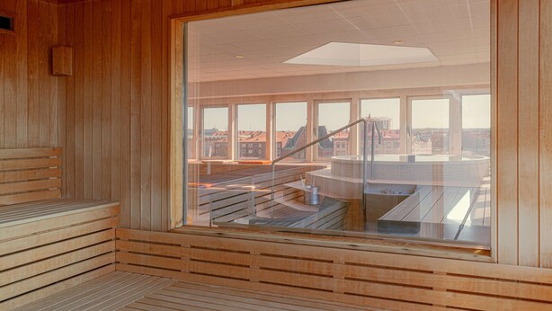 A wooden interior with a large window, a wooden bench, and a view of buildings outside. - Scandic Hallandia (Halmstad)