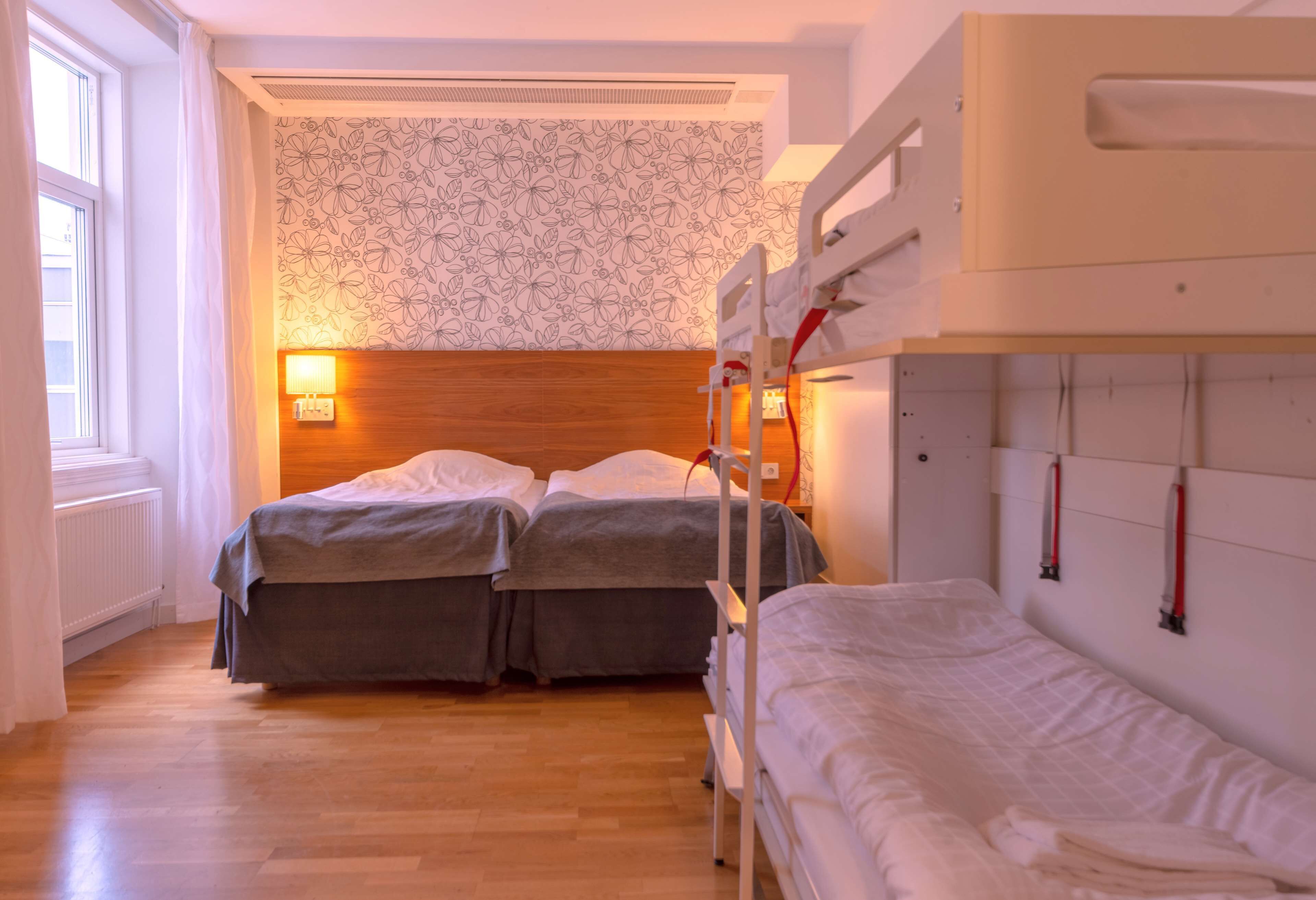 A hotel room with two beds, a wooden headboard, a patterned wall, and a window with curtains.