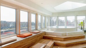 A modern spa area with a hot tub and seating by large windows overlooking a cityscape. - Scandic Hallandia (Halmstad)