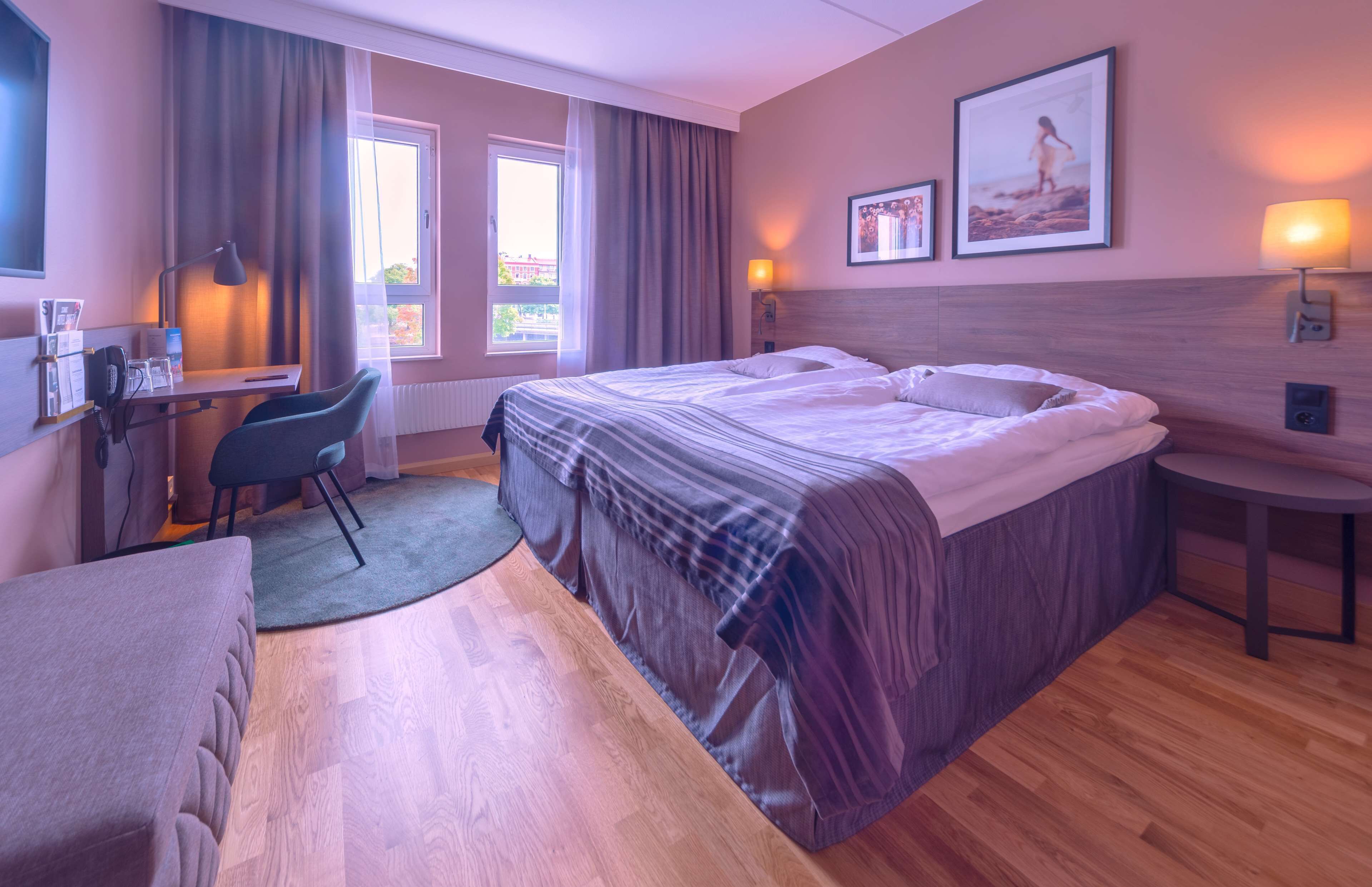 A hotel room with a bed, desk, chair, and a view of the outdoors.