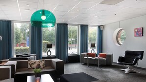 A modern hotel lobby with a sofa set, a round table, a black leather chair, and large windows with blue curtains. - Scandic Hallandia (Halmstad)