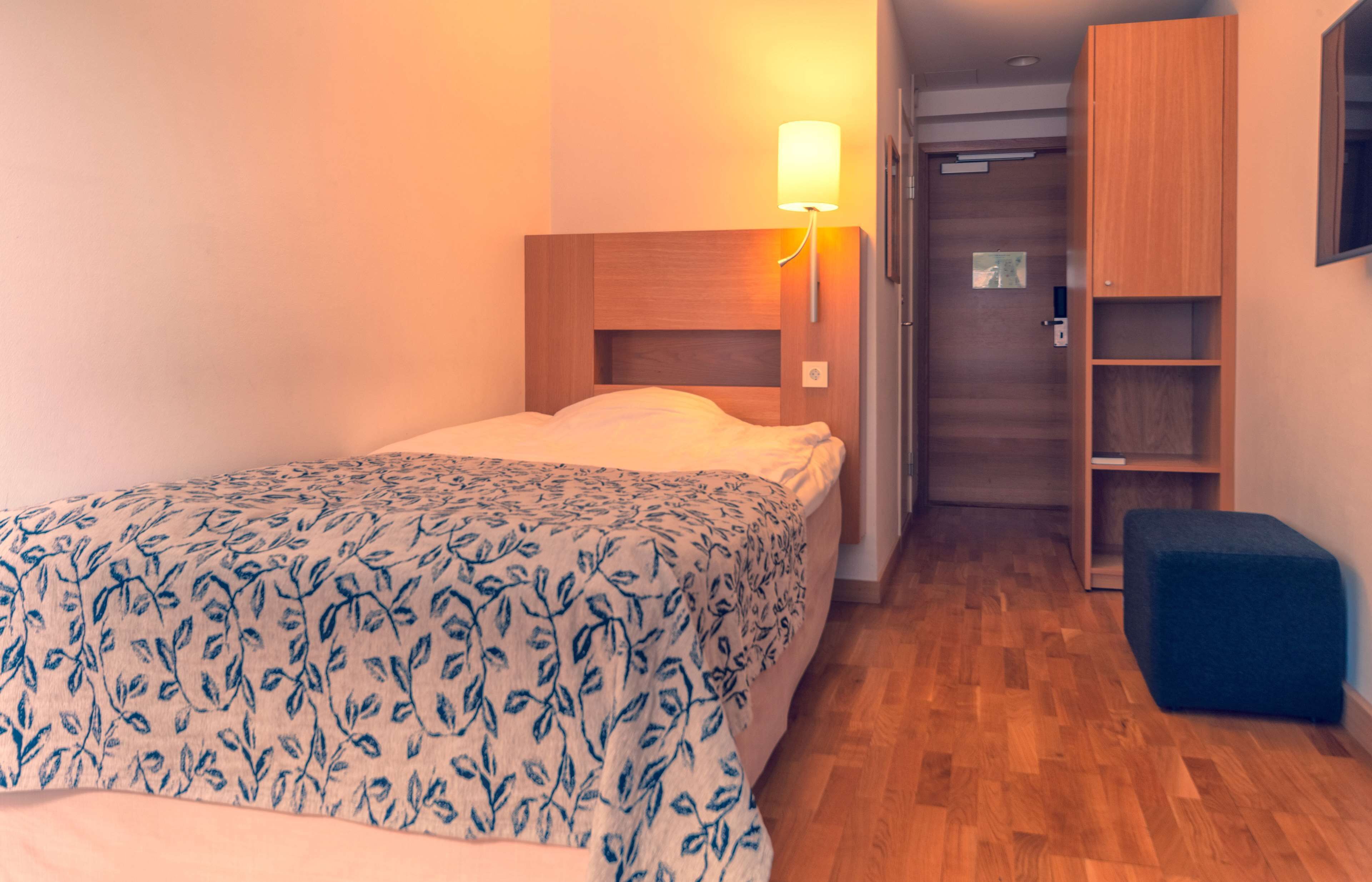 Une chambre à coucher comprenant un lit, une lampe de chevet, une armoire et un petit pouf.