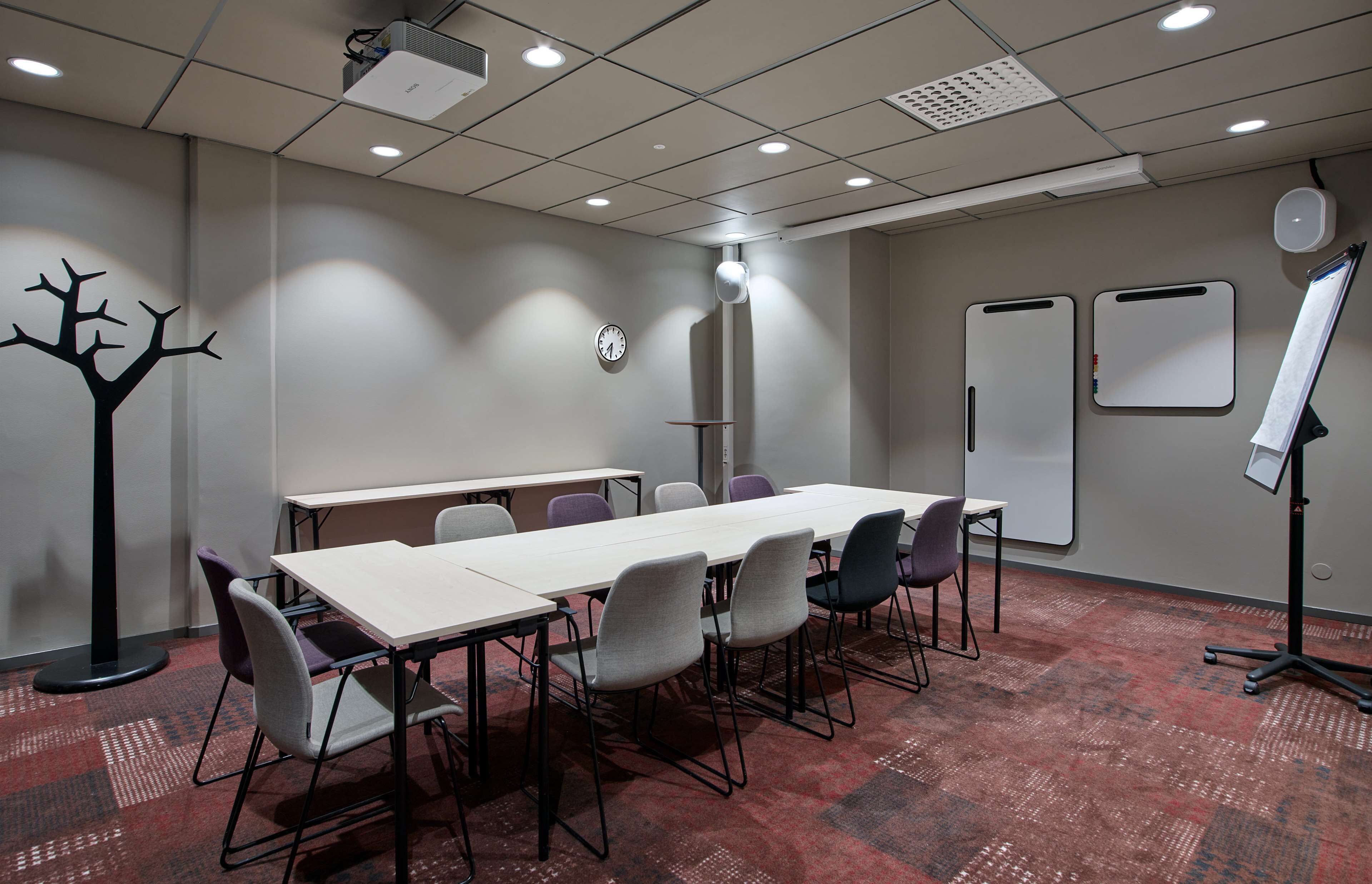 A conference room with a long table, chairs, a clock, a whiteboard, and a projector.